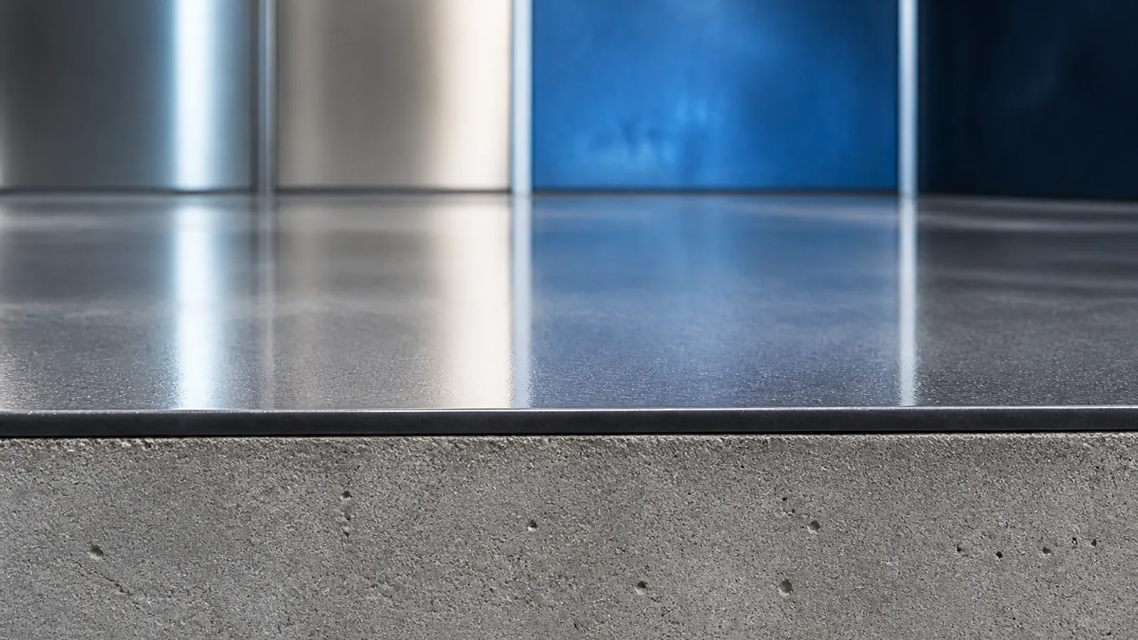 Close-up of a floor edge showing a thick matte grey cement base with a very thin glossy charcoal epoxy coating on top