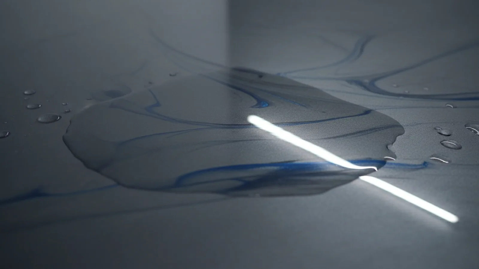 Water pooling in a thin film across a high-gloss charcoal epoxy floor, the reflective surface showing how liquid sits on top of the non-porous coating